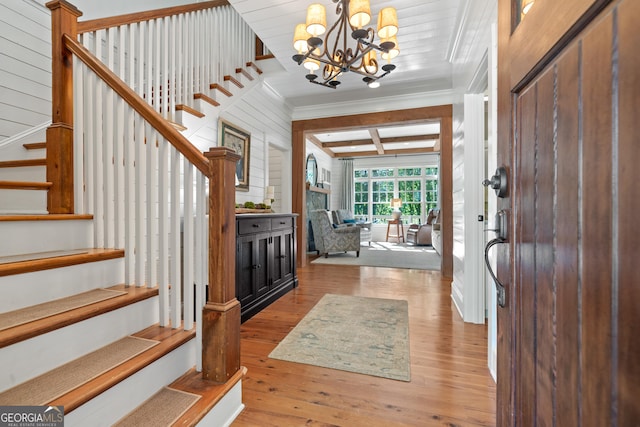 foyer featuring stairway, hardwood / wood-style floors, coffered ceiling, ornamental molding, and a chandelier