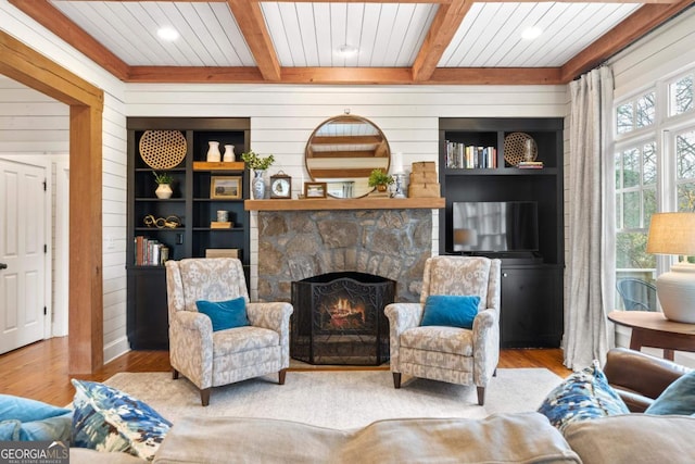 living room featuring beamed ceiling, a fireplace, wooden walls, and light hardwood / wood-style flooring