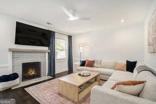 living room with a brick fireplace, ceiling fan, and dark wood-type flooring