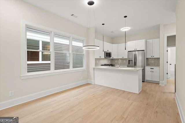 kitchen with white cabinetry, kitchen peninsula, decorative light fixtures, decorative backsplash, and appliances with stainless steel finishes