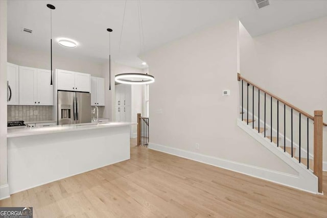 kitchen featuring tasteful backsplash, stainless steel refrigerator with ice dispenser, decorative light fixtures, white cabinets, and light wood-type flooring