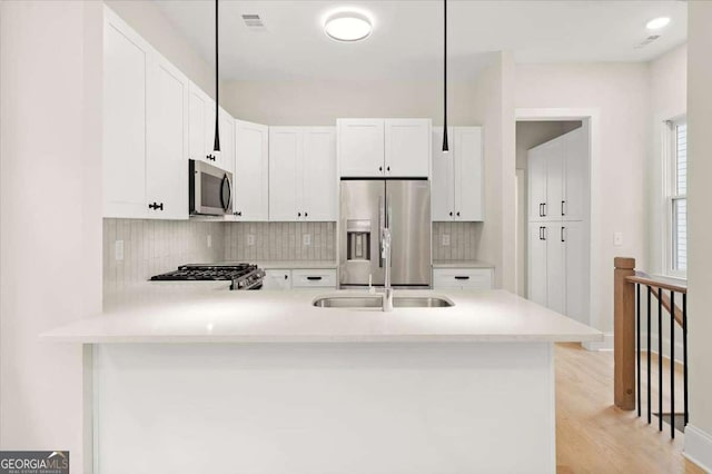 kitchen featuring appliances with stainless steel finishes, light wood-type flooring, sink, white cabinetry, and hanging light fixtures