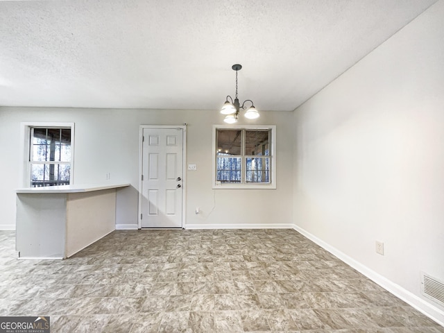 unfurnished dining area featuring a notable chandelier and a textured ceiling