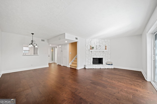 unfurnished living room featuring dark hardwood / wood-style flooring, a fireplace, a textured ceiling, and an inviting chandelier