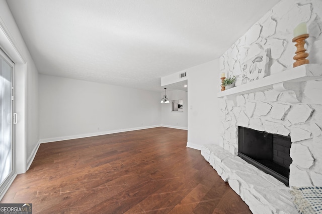 unfurnished living room featuring a stone fireplace, dark wood-type flooring, and a chandelier