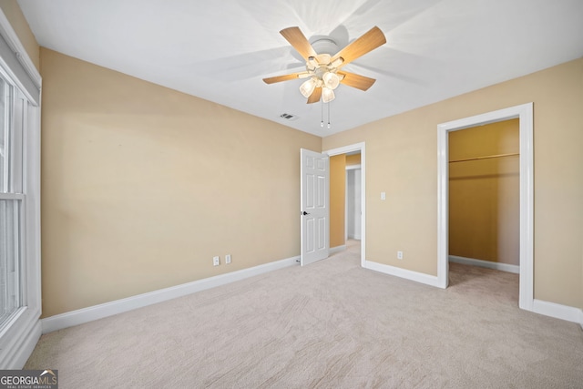 unfurnished bedroom featuring ceiling fan, a spacious closet, light carpet, and a closet