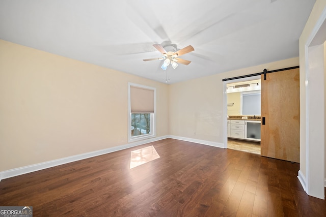 unfurnished bedroom with sink, hardwood / wood-style flooring, ceiling fan, a barn door, and connected bathroom