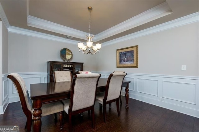 dining room with a raised ceiling, dark hardwood / wood-style flooring, ornamental molding, and an inviting chandelier