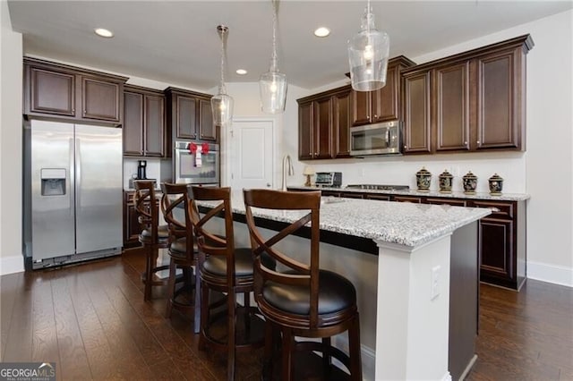 kitchen featuring pendant lighting, a breakfast bar, an island with sink, appliances with stainless steel finishes, and dark hardwood / wood-style flooring