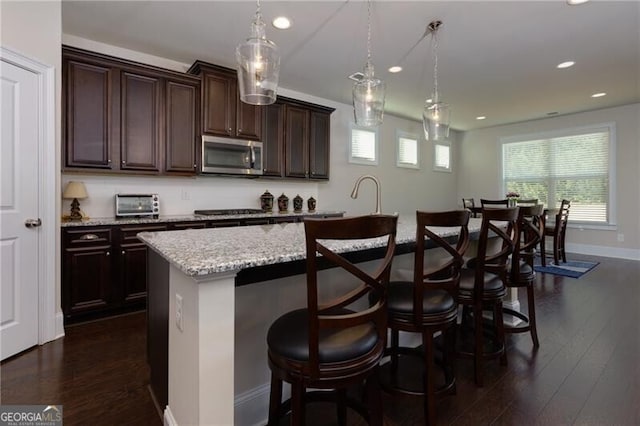 kitchen with a center island with sink, a kitchen bar, hanging light fixtures, and appliances with stainless steel finishes