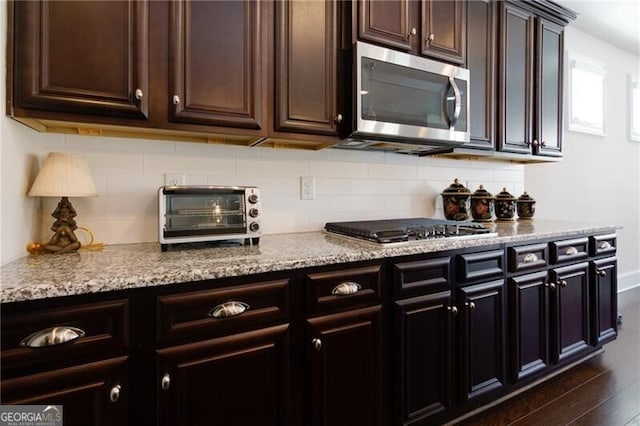 kitchen featuring dark hardwood / wood-style flooring, light stone countertops, dark brown cabinetry, and appliances with stainless steel finishes