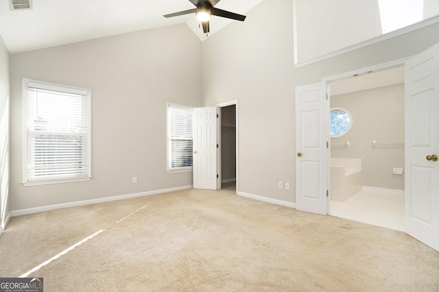 unfurnished bedroom with ceiling fan, light colored carpet, a walk in closet, and high vaulted ceiling