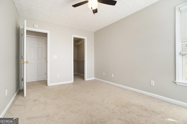 unfurnished bedroom featuring a walk in closet, a textured ceiling, light colored carpet, ceiling fan, and a closet