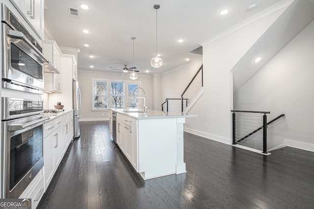 kitchen with stainless steel appliances, a kitchen island with sink, sink, white cabinetry, and hanging light fixtures