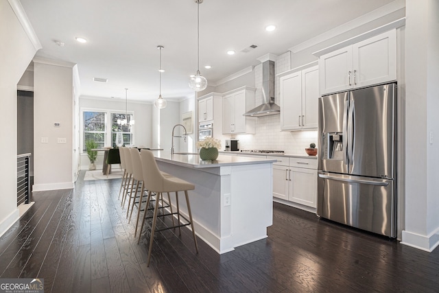 kitchen featuring appliances with stainless steel finishes, white cabinetry, a kitchen island with sink, and wall chimney exhaust hood