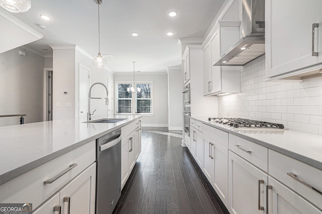 kitchen with stainless steel appliances, sink, wall chimney range hood, white cabinetry, and hanging light fixtures