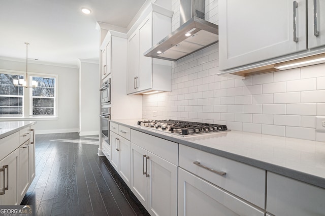 kitchen featuring wall chimney exhaust hood, pendant lighting, stainless steel gas stovetop, white cabinets, and ornamental molding