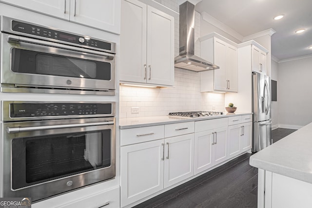 kitchen featuring crown molding, wall chimney exhaust hood, dark hardwood / wood-style floors, appliances with stainless steel finishes, and white cabinetry