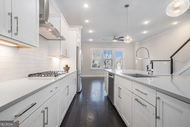 kitchen with pendant lighting, white cabinets, wall chimney range hood, sink, and stainless steel appliances