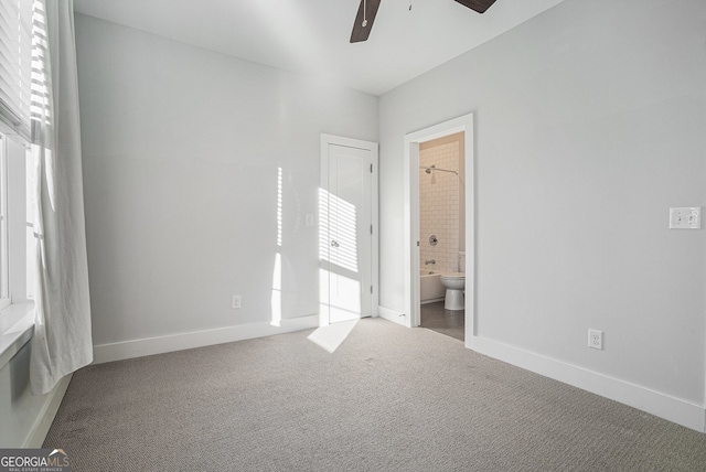 unfurnished bedroom with dark colored carpet, connected bathroom, multiple windows, and ceiling fan