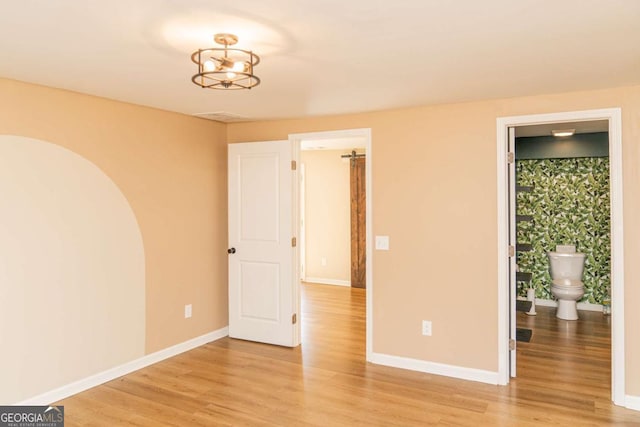 unfurnished bedroom featuring a chandelier, light hardwood / wood-style floors, and connected bathroom