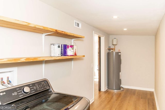 clothes washing area featuring electric water heater, light hardwood / wood-style floors, and washer / clothes dryer