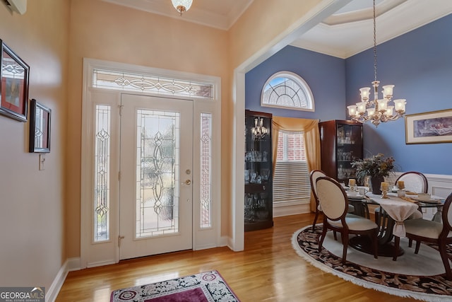 foyer entrance with a healthy amount of sunlight, light wood-type flooring, crown molding, and a chandelier