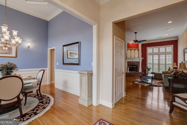 dining space with ornamental molding, light hardwood / wood-style floors, ceiling fan with notable chandelier, and a brick fireplace