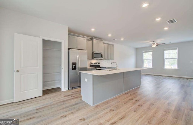 kitchen featuring appliances with stainless steel finishes, light hardwood / wood-style floors, a kitchen island with sink, and gray cabinetry