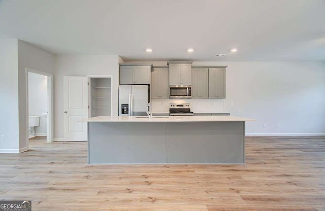 kitchen with gray cabinetry, a center island with sink, light wood-type flooring, and appliances with stainless steel finishes