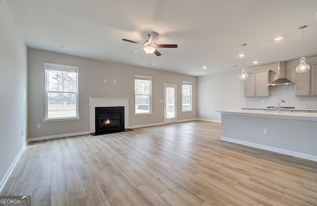 unfurnished living room with light wood-type flooring, ceiling fan, and sink