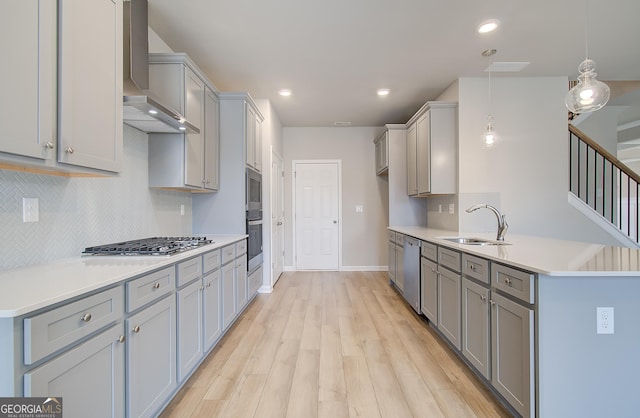 kitchen with sink, light hardwood / wood-style flooring, wall chimney exhaust hood, appliances with stainless steel finishes, and decorative light fixtures