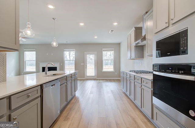 kitchen with gray cabinetry, sink, decorative light fixtures, appliances with stainless steel finishes, and light wood-type flooring