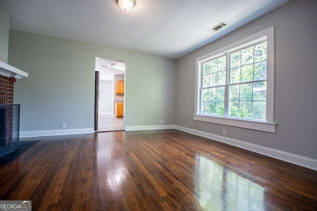 unfurnished living room with dark wood-type flooring and a brick fireplace