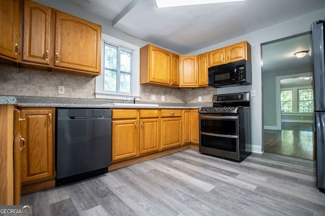 kitchen with tasteful backsplash, sink, black appliances, and light wood-type flooring