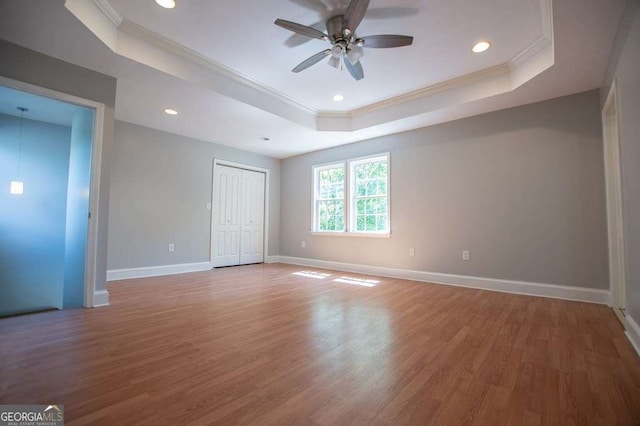 spare room featuring a raised ceiling, ceiling fan, wood-type flooring, and ornamental molding