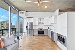 kitchen featuring white cabinets, sink, wall chimney exhaust hood, appliances with stainless steel finishes, and a wall of windows