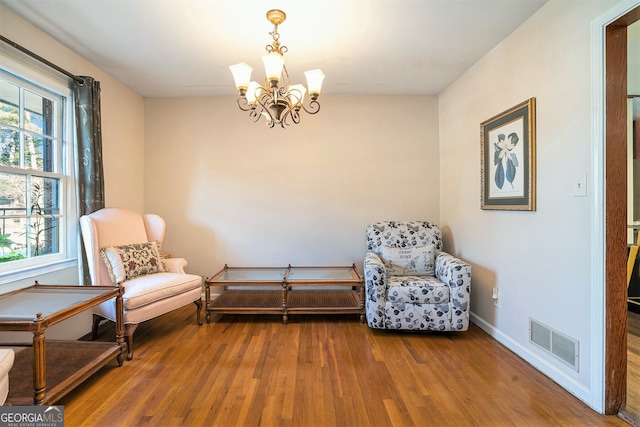 living area featuring visible vents, a notable chandelier, baseboards, and wood finished floors