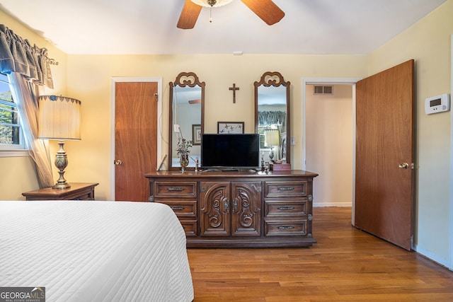 bedroom with a ceiling fan, wood finished floors, visible vents, and baseboards