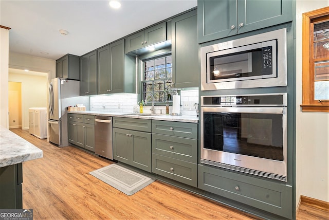 kitchen with stainless steel appliances, a sink, light countertops, light wood-type flooring, and decorative backsplash