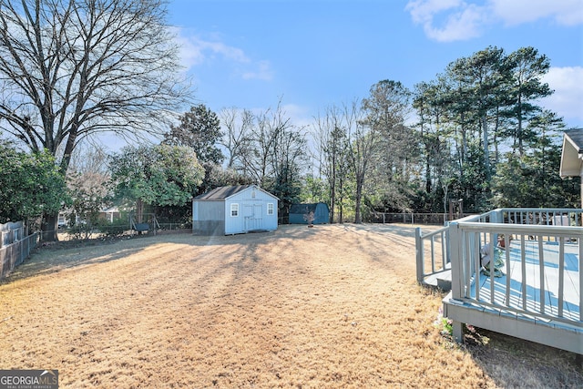 view of yard with a shed, a wooden deck, a fenced backyard, and an outbuilding