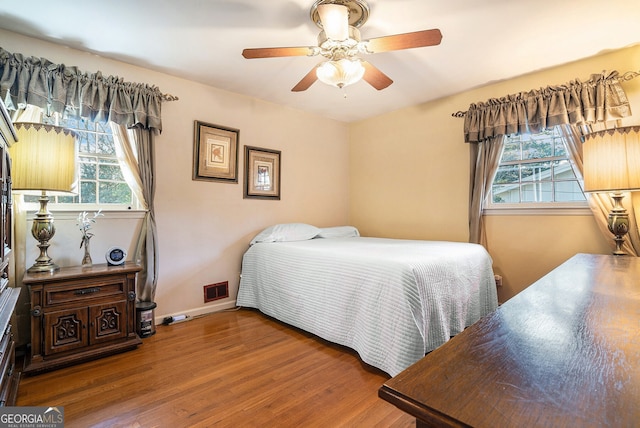 bedroom with ceiling fan, wood finished floors, visible vents, and baseboards