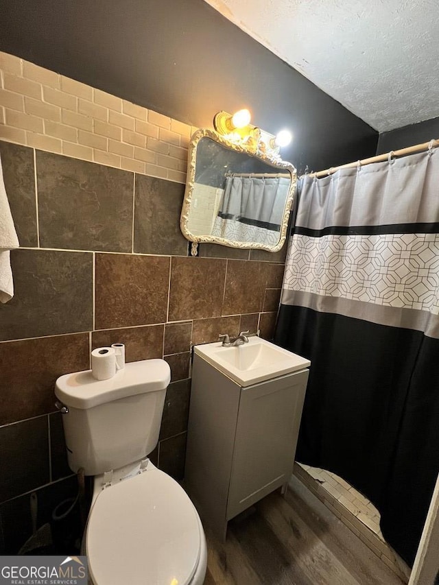 bathroom with hardwood / wood-style floors, vanity, toilet, a textured ceiling, and tile walls