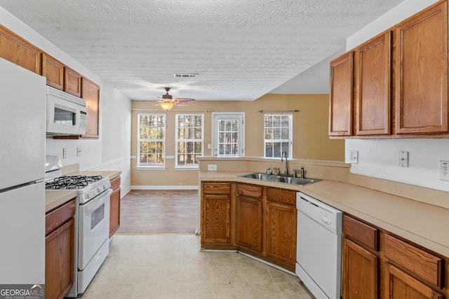 kitchen featuring white appliances, sink, ceiling fan, a textured ceiling, and kitchen peninsula