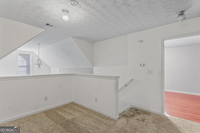 additional living space featuring a textured ceiling, lofted ceiling, and light carpet