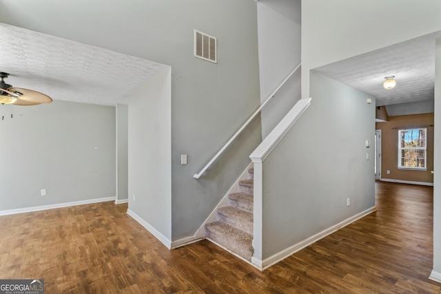 stairway featuring ceiling fan, wood-type flooring, and a textured ceiling