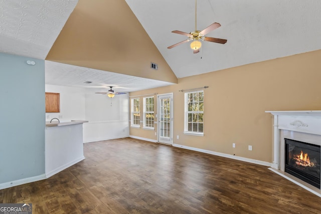 unfurnished living room featuring a textured ceiling, ceiling fan, dark wood-type flooring, and high vaulted ceiling