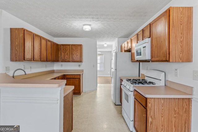 kitchen featuring a textured ceiling, kitchen peninsula, and white appliances