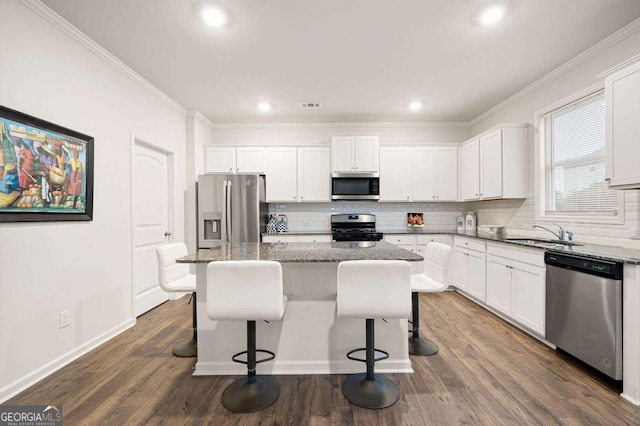 kitchen featuring a kitchen island, white cabinetry, stainless steel appliances, and dark stone counters