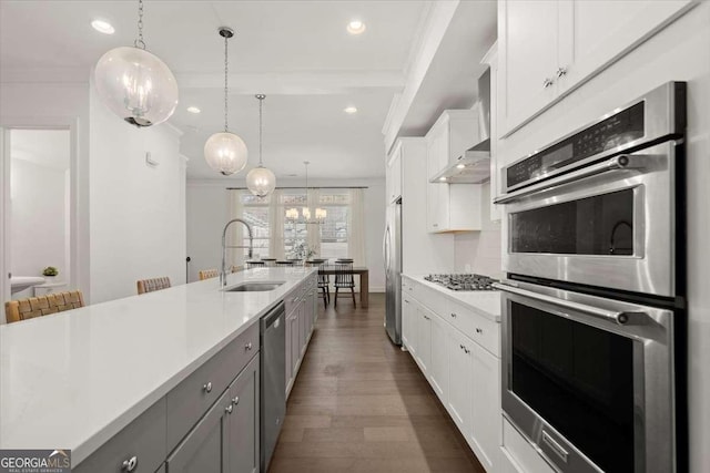 kitchen with appliances with stainless steel finishes, sink, a large island with sink, white cabinets, and hanging light fixtures